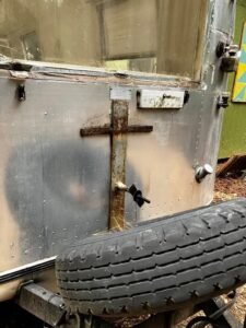 A rusted cross-shaped bracket on the back of the trailer, above the spare tire