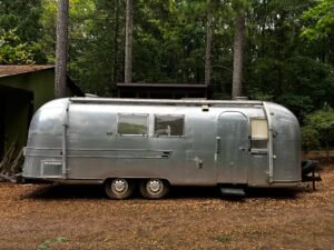 The 1967 Airstream side-on, parked among pine trees