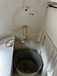 The shower corner as it is now: a galvanized tub under old taps and hoses